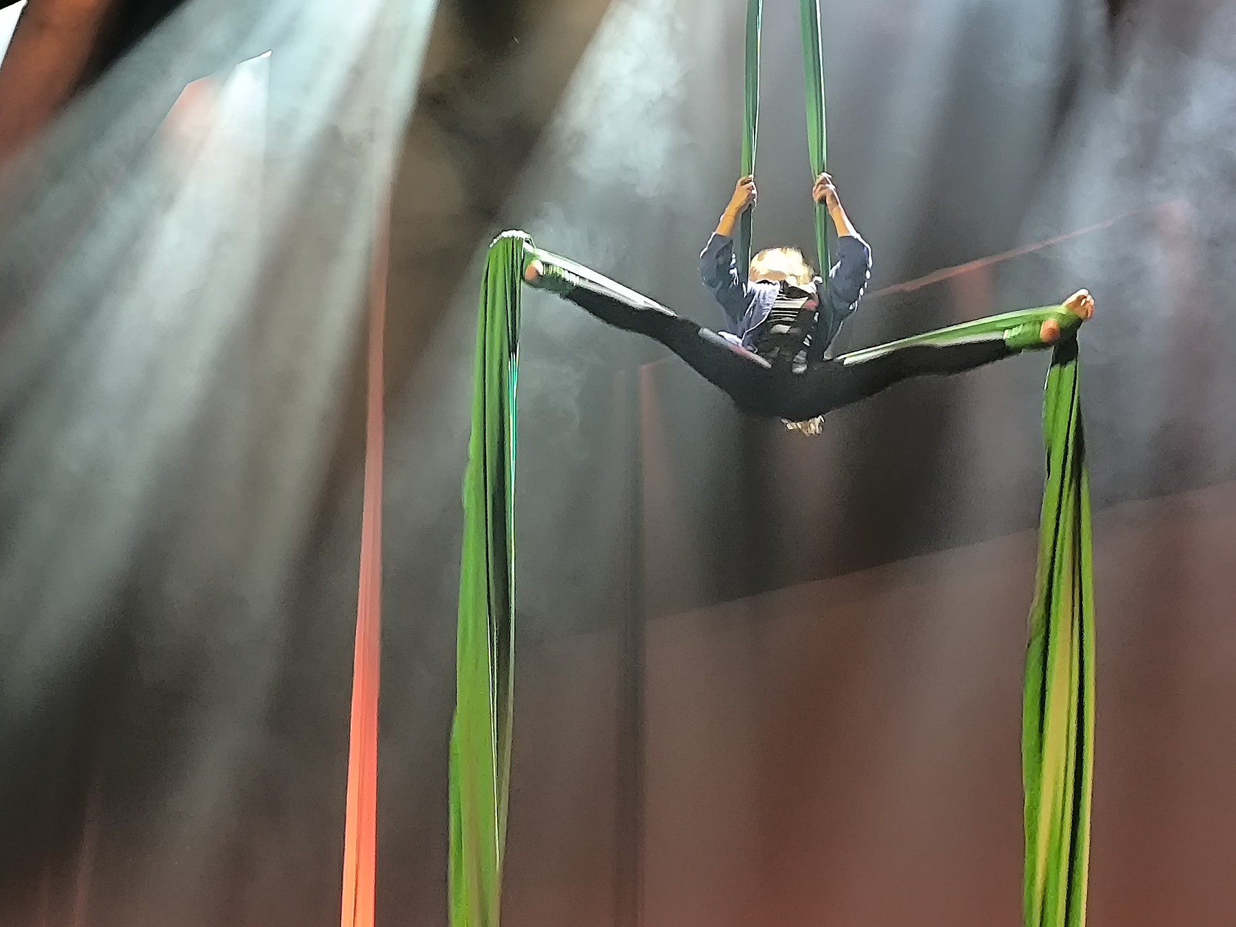 Vertikalartistin an bunten Vertikaltüchern in dramatischem Bühnenlicht