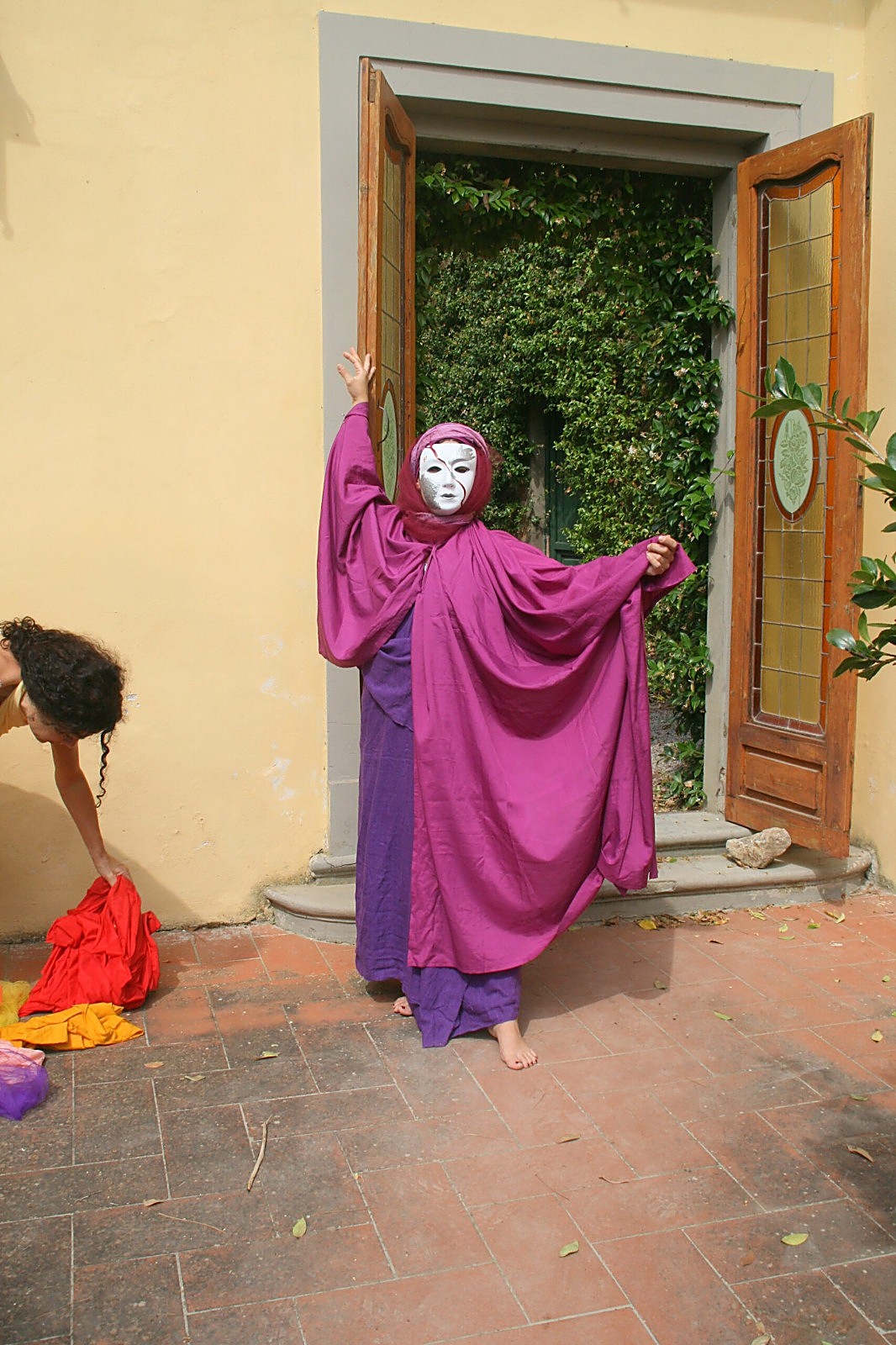 Theaterspielerin in violettem Umhang mit Maske vor einer grünen Tür